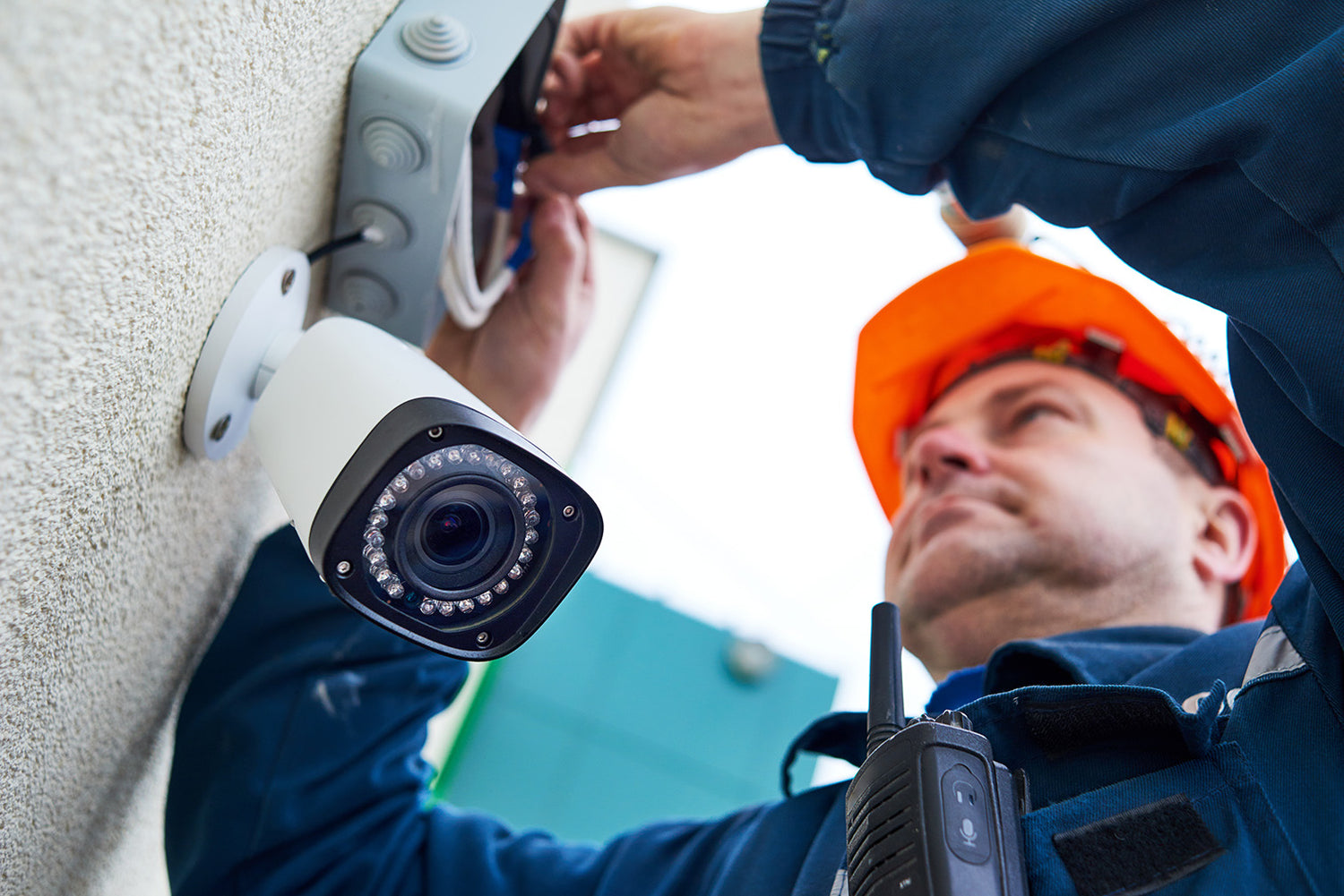 A man in a hardhat performing maintenance on a security camera