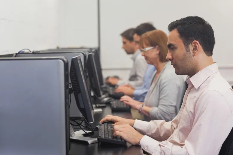 A group of people typing on keybaords in front of a row of computers