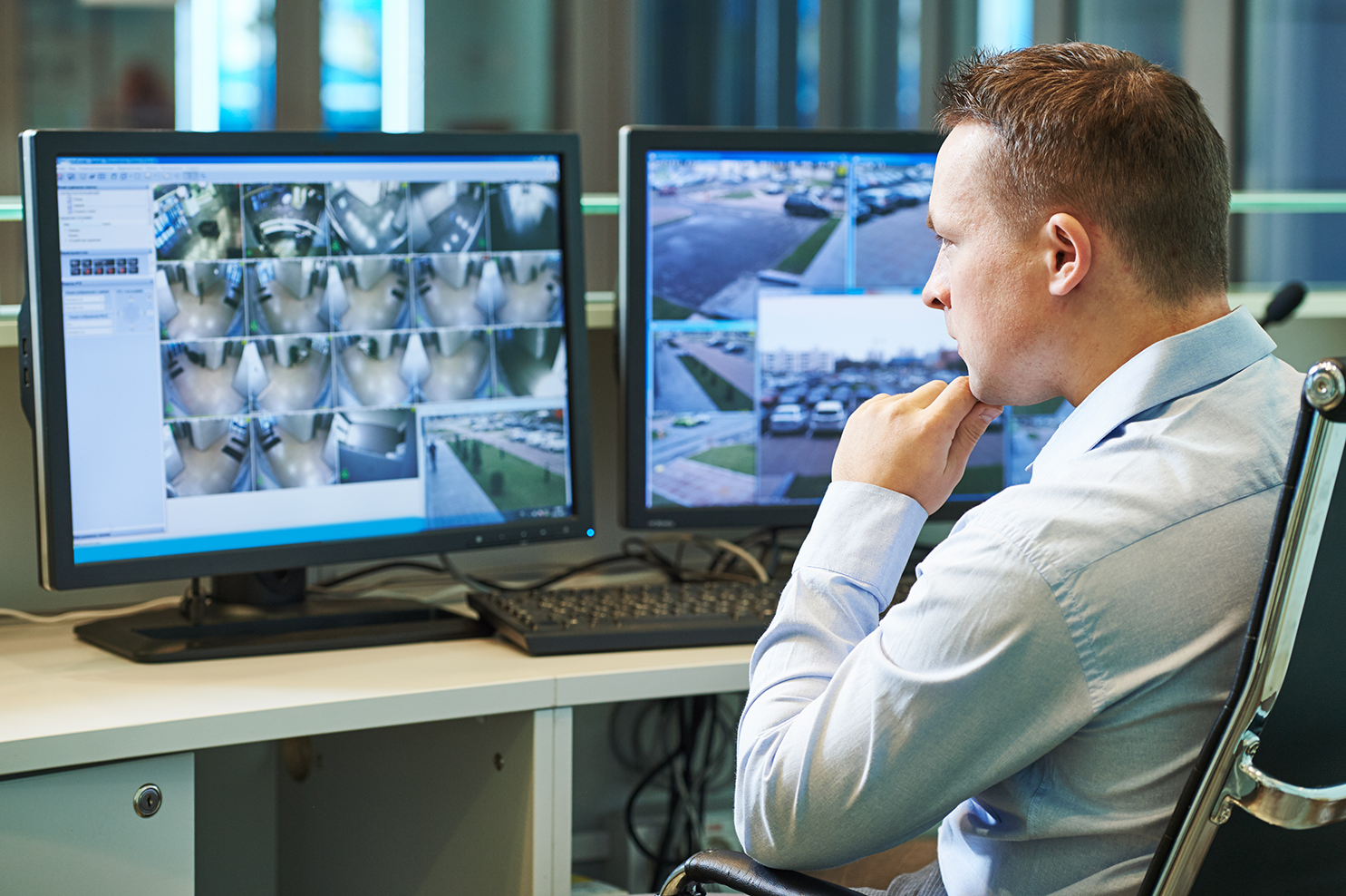 A man sitting at a desk in front of computer monitors showing security footage