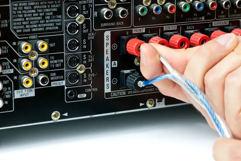 A hand holding wires in the back of a speaker system unit