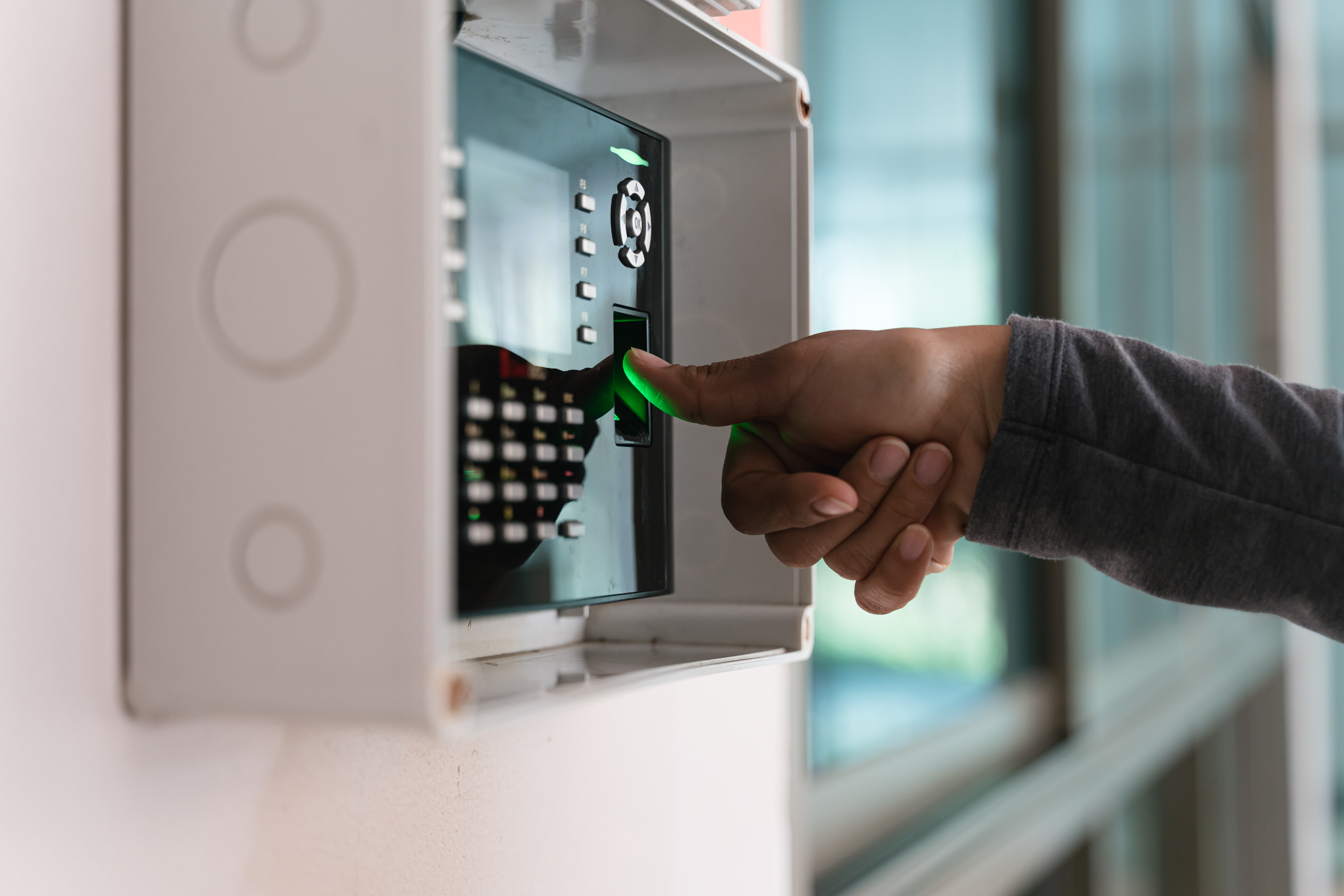 A hand holding a finger to a thumbprint scanner on a panel